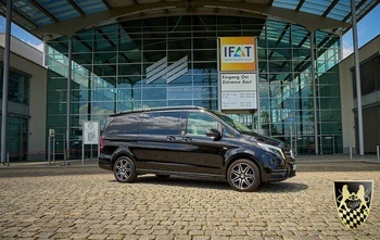 In the image, a sleek black limousine is parked outside a modern event venue in München, ready to provide first-class event shuttle services. Guests are arriving and being greeted by professional chauffeurs, showcasing the comfort and reliability of the event shuttle service.