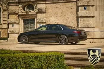 München Garmisch-Partenkirchen Transfer 7 Ein eleganter Chauffeur in einem Anzug hält die Tür einer Limousine offen, während im Hintergrund die beeindruckende Alpenlandschaft von Garmisch-Partenkirchen mit der Zugspitze zu sehen ist. Diese Szene vermittelt ein Gefühl von Luxus und Sicherheit, ideal für Kunden, die einen Flughafentransfer oder eine stilvolle Fahrt in die Berge planen.